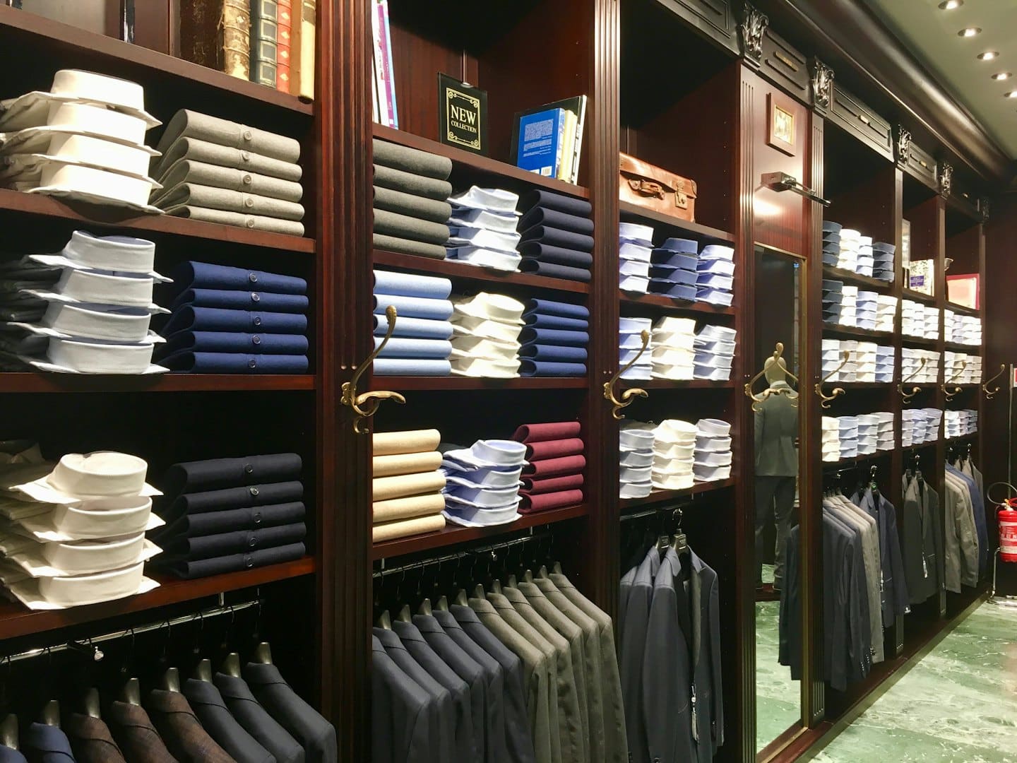 Abbigliamento formale da uomo ordinatamente disposto su scaffali e appendiabiti del negozio.